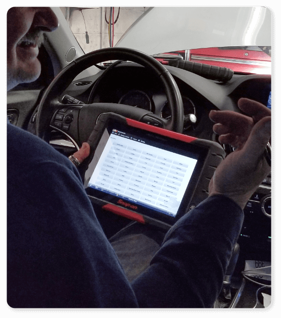 An auto technician at Hemlock Auto & Alignment using a diagnostics machine while sitting inside the car