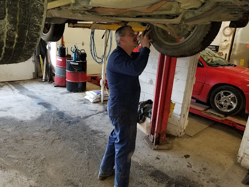 Brake Noise Guide by Hemlock Auto | Brake Repair in Hemlock, MI. Image of Hemlock Auto owner Dave Murdock inspecting the brakes on a car on lift in shop from underneath behind the tire.