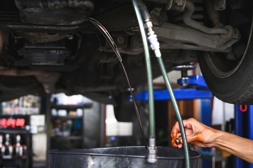 Transmission repair services near me in Hemlock, MI with Hemlock Auto and Alignment. Image of mechanic hand performing a transmission fluid change on vehicle is shop with tool to catch fluid.