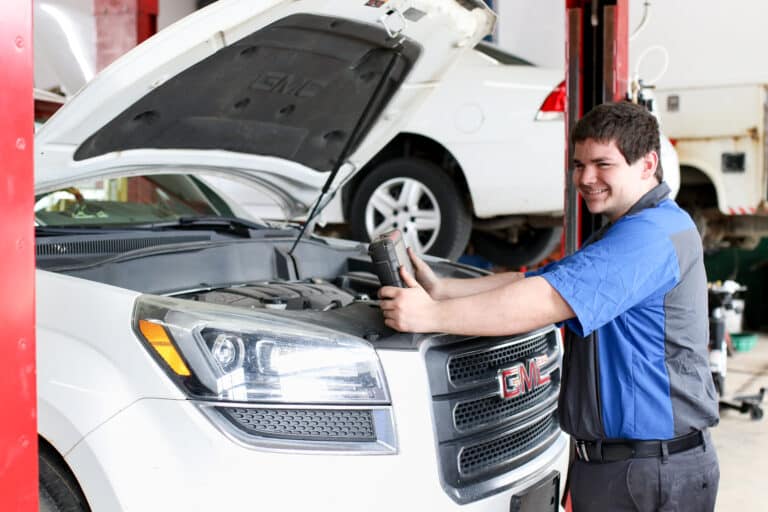 A technician at Hemlock Auto and Alignment in Hemlock, MI, diligently inspecting the engine of a gray car with its hood open, showcasing the commitment to quality car maintenance services.
