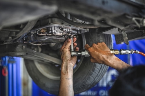 Automotive Transmission Repair and Service in Hemlock, MI at Hemlock Auto and Alignment. Image of a lifted car with a mechanic's hands performing repairs on the automotive transmission underneath the car in Hemlock, MI